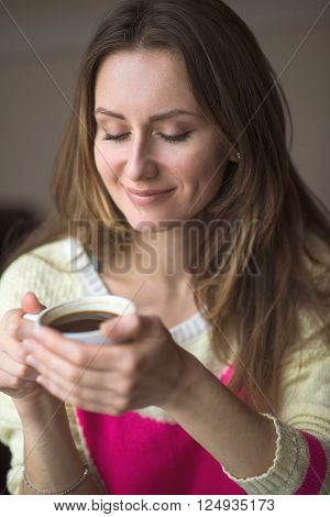 Young happy girl smiling and holding a cup of hot coffee or tea sits in a cafe, lifestyle, breakfast or dinner to spend time relaxing, healthy lifestyle, fashion, in a yellow sweater.