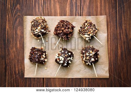 Frozen banana covered with chocolate and peanuts on paper over wooden background top view