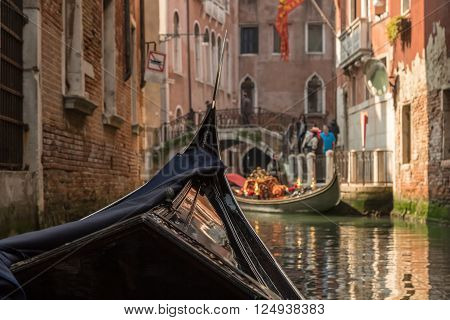 View of a bridge and another gondola shot from within a gondola on a canal in Venice on a bright sunny day showing front of the gondola in the foreground