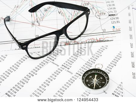 Glasses and compass on grpahical charts background, business concept