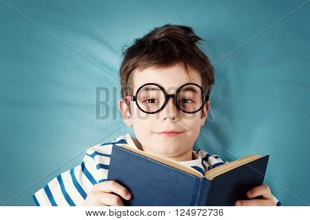 seven years old child lying with book on blue background
