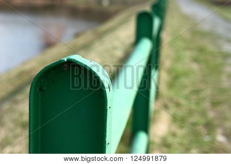 Green railing with blurred background - river and path on sunny day