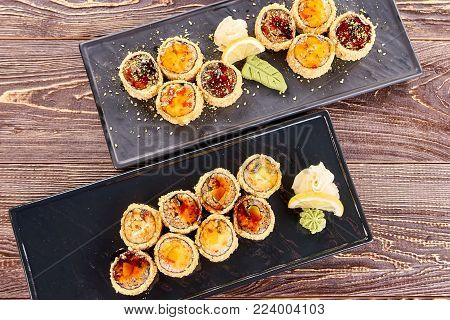 Two plates of juicy unagi furay sushi, top view. Sets of sushi with white ginger, wasabi and lemon.