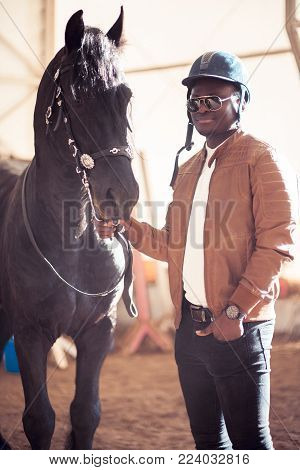 african Man wearing sunglasses near a black horse in hangar