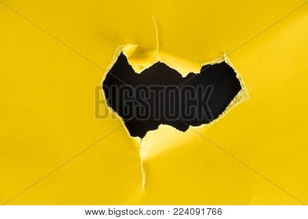 close-up shot of hole in yellow paper isolated on black