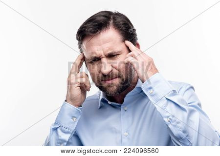 Throbbing pain. Pleasant middle-aged man in a baby blue shirt massaging the temples while wincing from a splitting headache