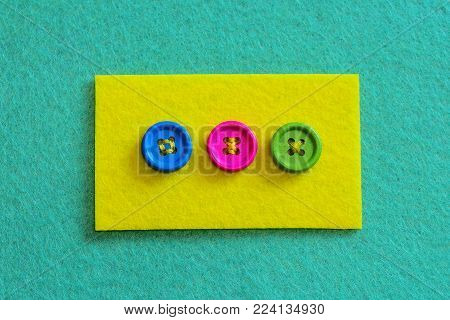 Different ways to sew buttons to felt. Felt piece with bright buttons isolated on felt background. Stitch buttons for sewing projects with colorful thread. Top view
