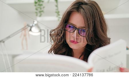 A young beautiful lady reading a book indoors. Close-up Dolly shot. Soft focus.