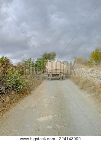 Narrow track with back view of lorry transporting large rocks in the countryside in Cyprus.