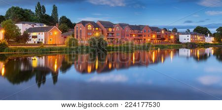 Street with residential buildings next to the river. Dusk. Street lighting. Exeter. Devon. England
