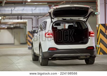 Modern white car with open trunk door at underground parking.