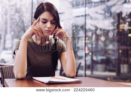 Difficult task. Meditative thoughtful female student massaging her temples while closing eyes and sitting in front of notebook