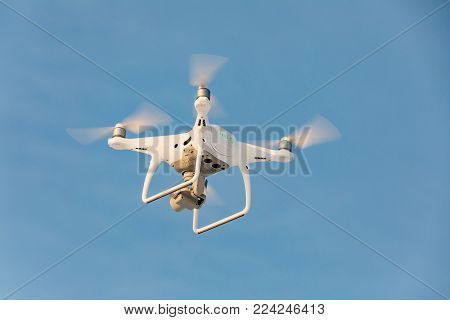 Flying white drone on the blue sky. Landing a droned hand with spinning propellers