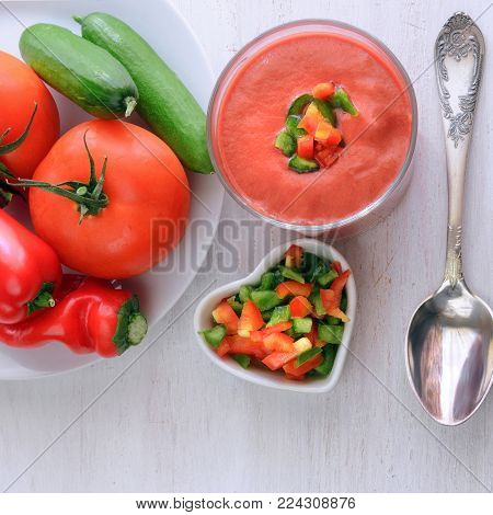 Gazpacho, tomato soup made from made of raw blended vegetables. Traditional Spanish cold soup in glass bowl on wooden table.