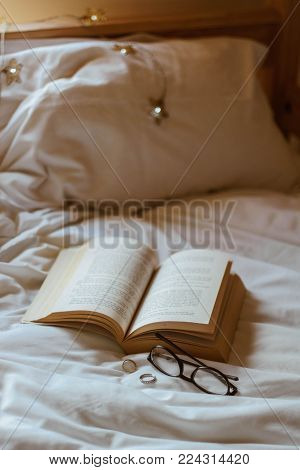Book on a bed with rings, glasses and fairylights