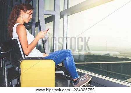 Woman carries your luggage at the airport terminal of Hong Kong, after gonna stady or education fly to Singapore. Use a mobile phone looking for flight