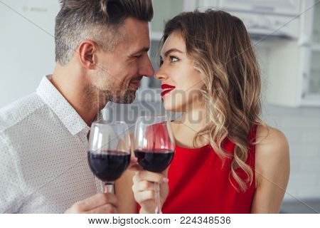 Portrait of a loving romantic smart dressed couple drinking red wine while celebrating Valentine's Day on a kitchen at home