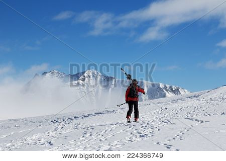 Skier with skis on his shoulder go up to top of mountain in cold sun day. Winter Caucasus Mountains in fog, Georgia, region Gudauri, Mt. Kudebi.