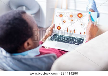 Statistic data. Handsome intelligent nice man holding a laptop and looking at the laptop screen while looking at the statistics