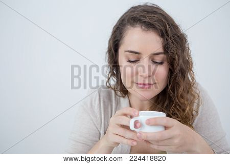 Closeup of content Caucasian woman holding white cup and looking at camera. Attractive young woman enjoying coffee. Tea or coffee break concept