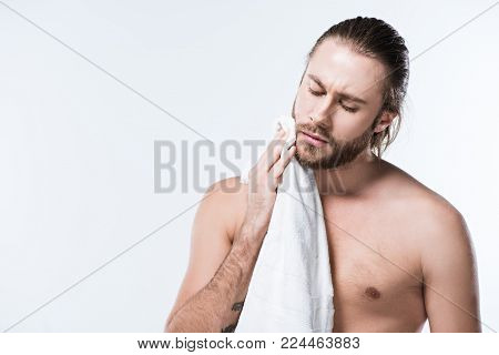 Bearded caucasian man with wet hair holding bath towel in hands while his eyes closed, isolated on white