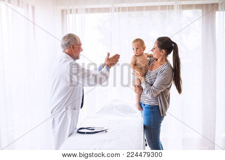 Senior male doctor , young mother and a baby boy in an office.
