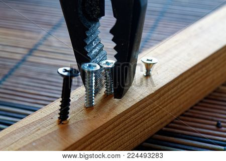 Scattered screws screwed into the wooden plank and pliers