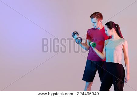 Sports girl and guy doing exercises. Keep dumbbells, train the biceps. Dark background, space for text.