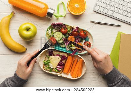 Healthy snack at office workplace. Businesswoman eating organic vegan meals from take away lunch box at wooden working table with computer keyboard