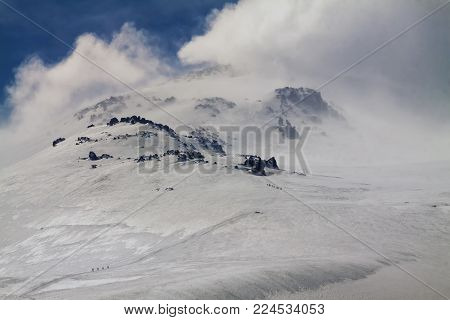 Groups of climbers during Mountain climbing . Wide icy slope, summit covered with clouds. Sunny windy day. Cold.