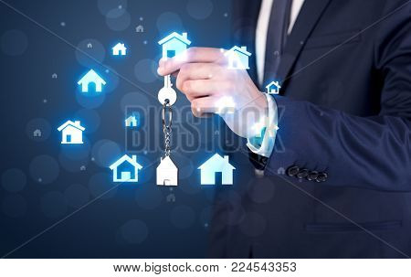 Businessman in suit holding keys with house graphics around and dark background