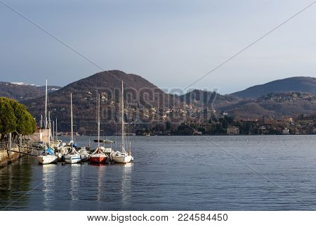 Sail boats moored along Lake Orta coast and Mottarone Hills covered of fresh snow