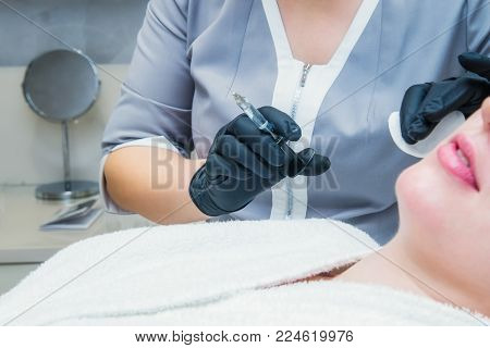 Contour plastic: Dermatologist doctor inject filler. Close up female hands of cosmetologist making injection in lips. Aesthetic cosmetology. Selective focus