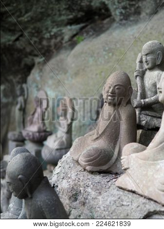 Ancient Buddhist arhat stone statue found in a small cave alcove on Mt. Nokogiri. Has a wonderful joyful expression on his face while seated in a yoga meditation position.