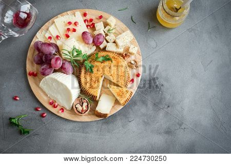 Cheese platter with assorted cheeses, grapes, nuts over gray stone background, copy space. Italian cheese and fruit platter.