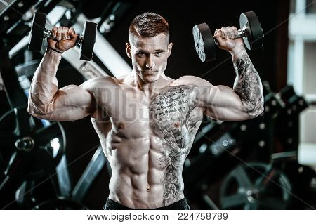 Handsome young muscular Caucasian man of model appearance working out training in the gym gaining weight pumping up muscles and poses fitness and bodybuilding concept