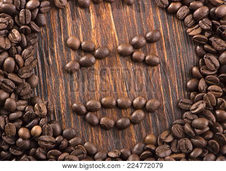 Smile shaped of roasted coffee beans on white wood background.