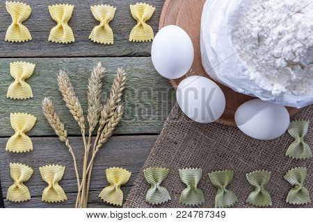 Spike of wheat, pasta, eggs and flour on a wooden background, with space for text.