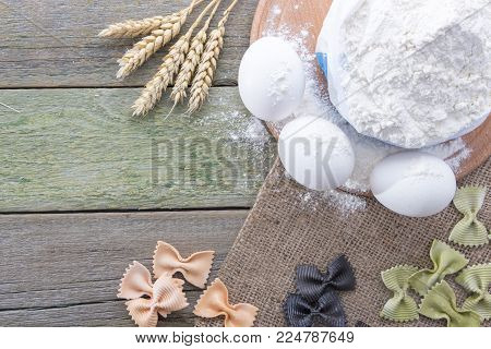Spike of wheat, pasta, eggs and flour on a wooden background, with space for text.