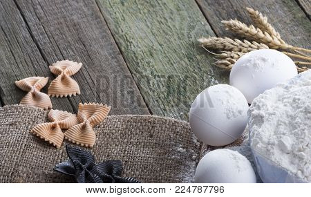 Spike of wheat, pasta, eggs and flour on a wooden background, with space for text.