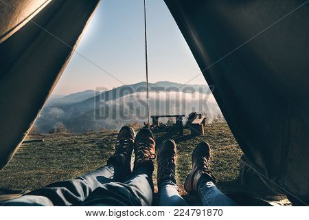 First they see in the morning. Close up of young couple enjoying the view of mountain range while lying in their tent