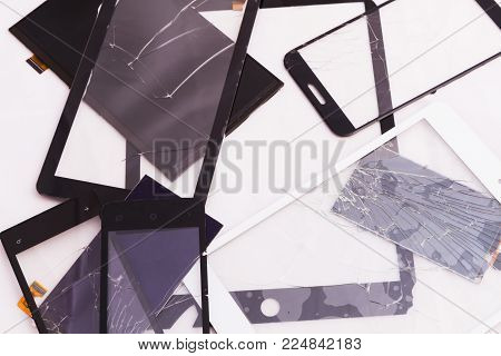 Broken touchscreen pile lying around a different size on a white background. On the glasses are cracked from the impact. Display and loops. High-tech product