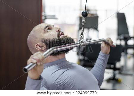 Male athlete doing exercises on pulldown machine in the gym, healthy lifestyle
