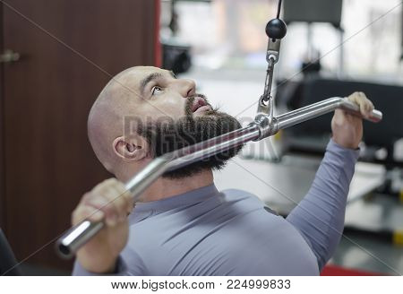 Motivated fit sportsman working hard at fitness club, doing pulldown exercises
