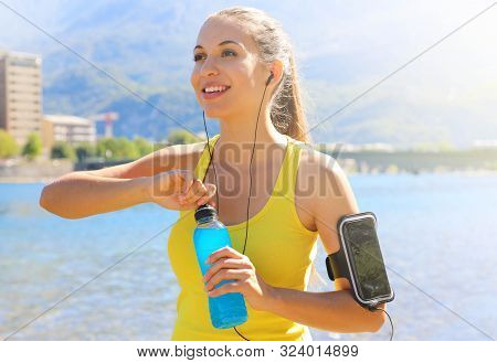 Happy Cheerful Female Athlete With Armband For Smart Phone Open Power Drink Bottle After Daily Train