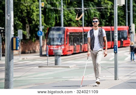Young Blind Man With White Cane Walking Across The Street In City.