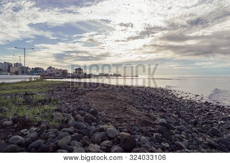 Cityscape Of Jeju Island From Lavarock Sea Shore At Sunset With Scenic Cloudscape On Background