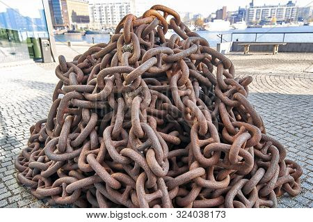 Old Chain On The Background Of The Pier. Rusty Anchor Chain Piled Up On The Pier, Close-up