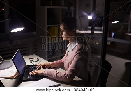 Young Businesswoman Siting At Her Workplace Typing On Laptop Computer And Working Online Till Late A