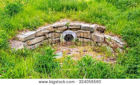 Stone Drain And A Round Metal Grid With Dry Leaves In A Park Surrounded By Green Vegetation, Wonderf